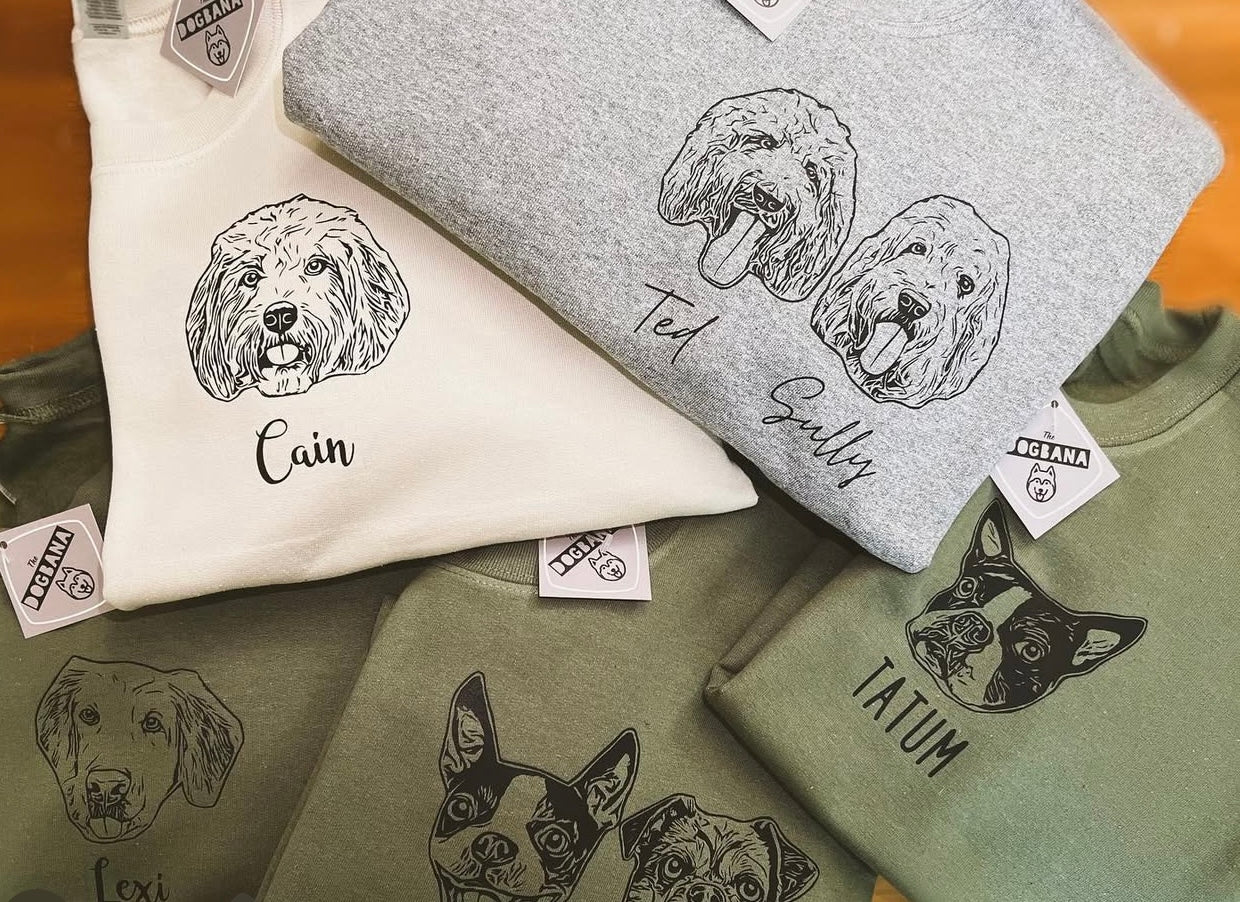 Crewnecks with dog illustrations and names on a wooden surface
